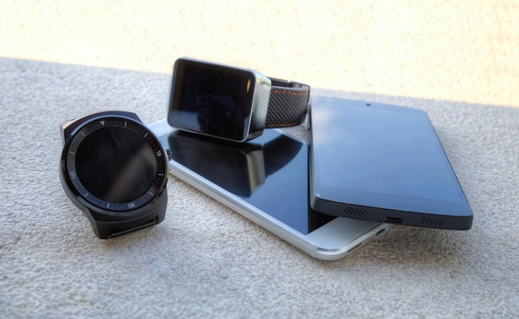 Various smart devices including smartwatches and smartphones placed on a textured surface